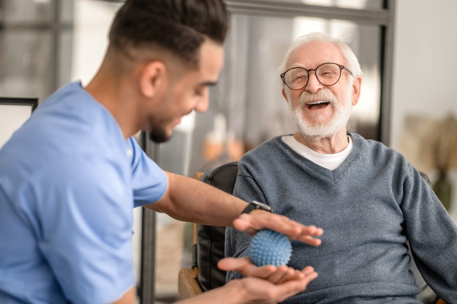 A caregiver and an older resident laughing together during a therapy session
